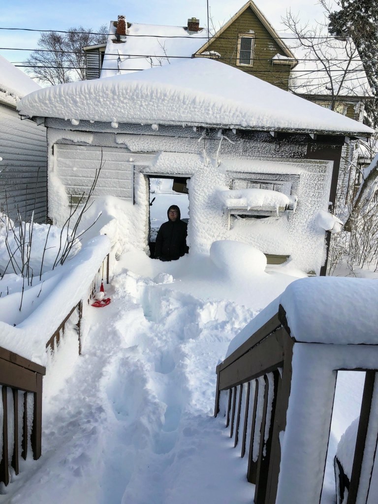 View of our garage with snow drifts obscuring about half of it.